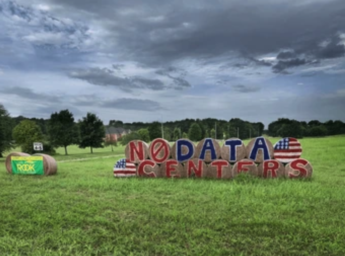 Round hay bales in a green field painted with American flags and the words No Data Centers